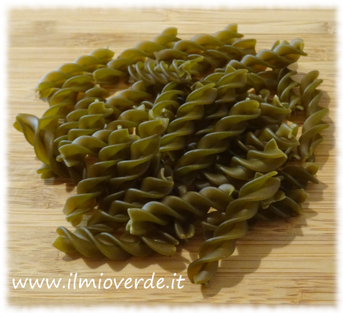 Fusilli di piselli verdi disposti su un tagliere di legno chiaro, illuminati da luce naturale.