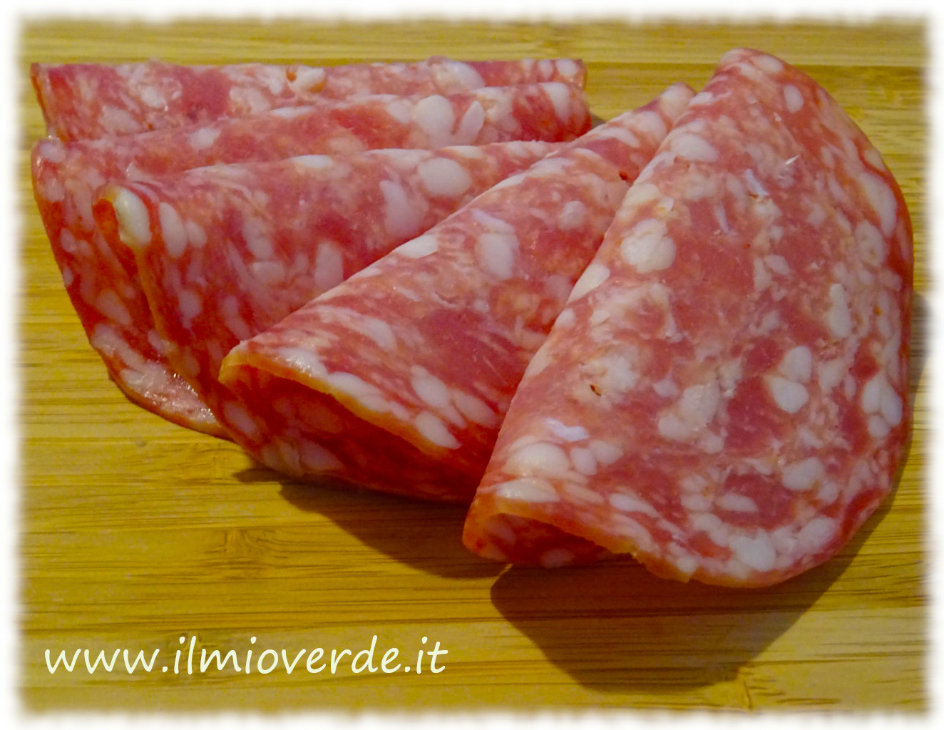 Tre fette di salame di Napoli su un tagliere di legno chiaro.