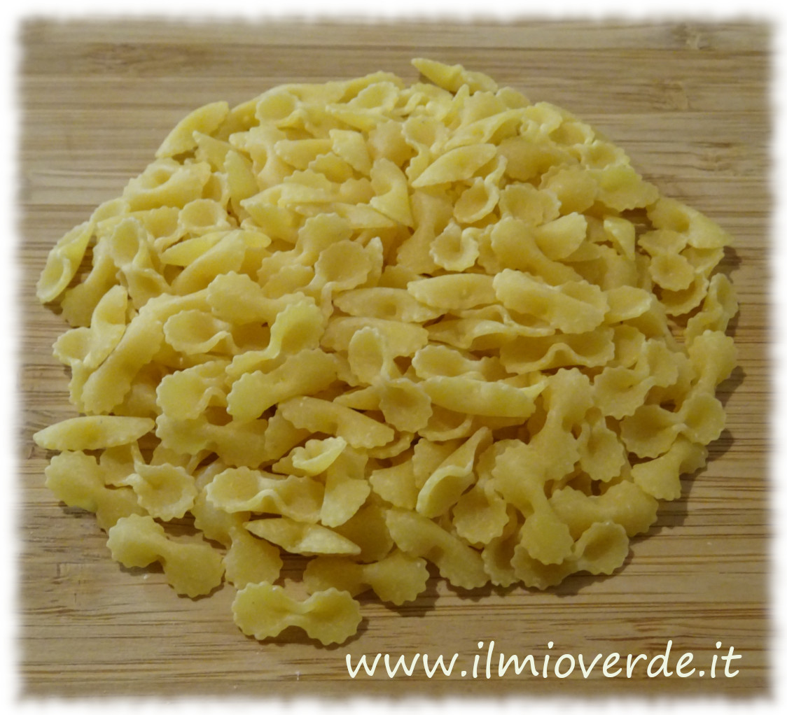 Farfalline all'uovo adagiate su un tagliere di legno, pronte per essere cucinate.
