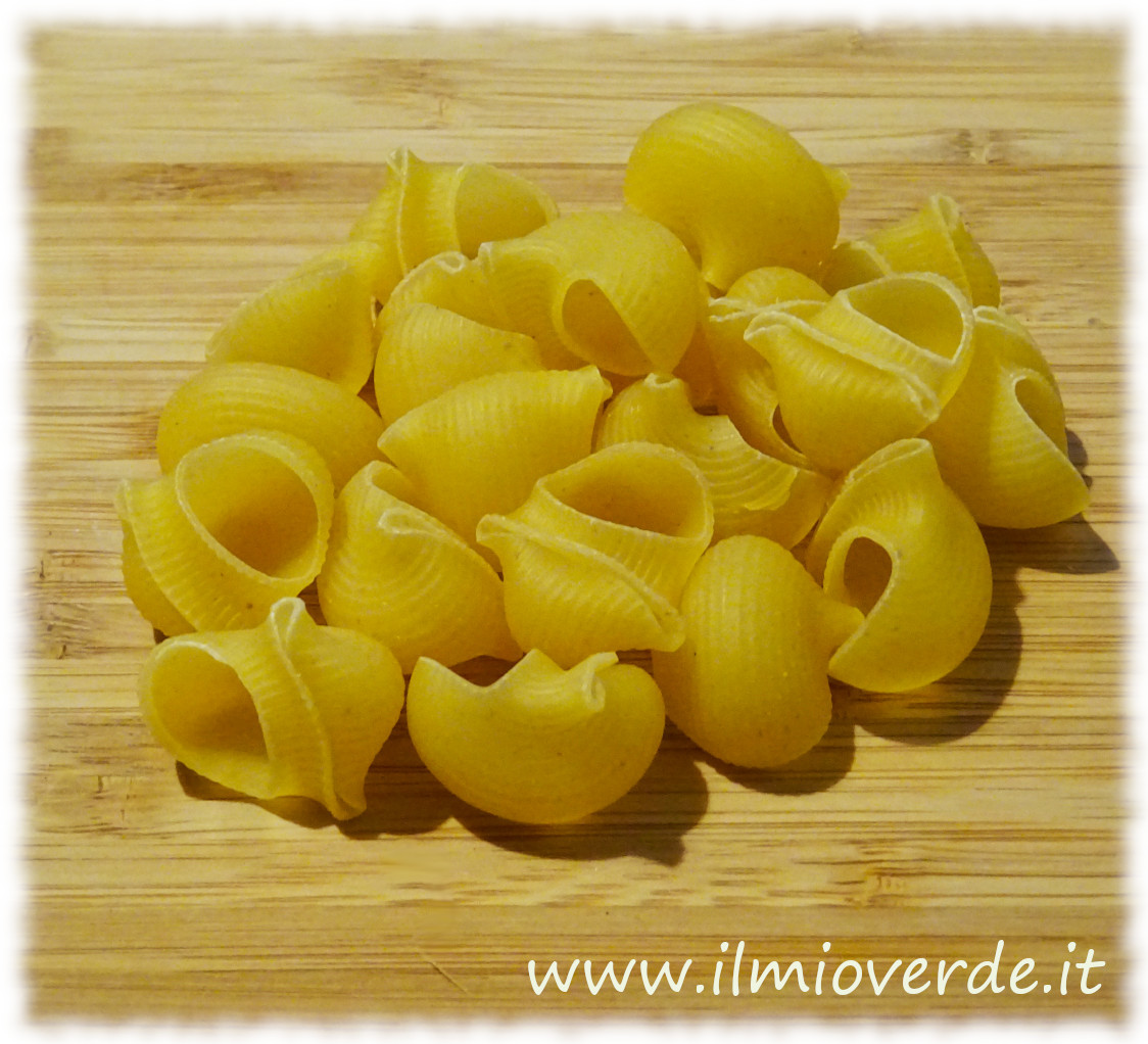 Una manciata di pipe rigate disposte su un tagliere di legno, pronte per essere cucinate.