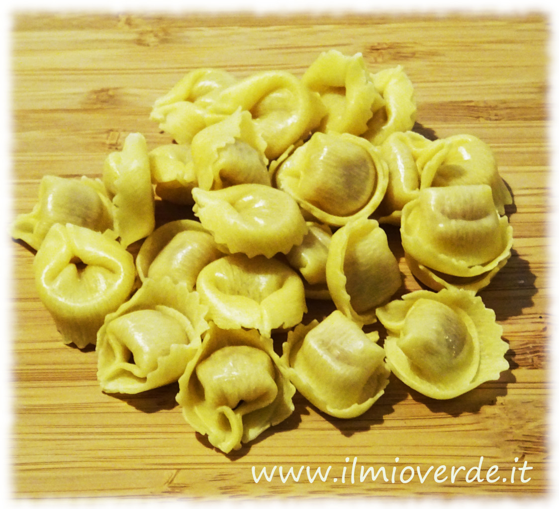 Tortellini freschi disposti su un tagliere di legno, pronti per essere cucinati.
